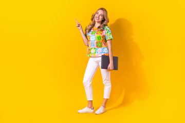 Full length photo of dreamy pretty woman dressed flower print t-shirt showing looking empty space holding gadget isolated yellow color background