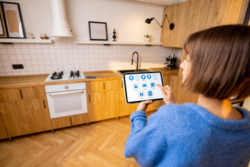Fototapeta na wymiar Woman holds a digital tablet with running smart home program, controlling smart kitchen appliances. Concept of new technologies for comfort living