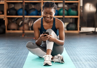 Fototapeta Happy black woman, fitness and phone for social media, communication or networking at the gym. African female person or athlete typing, texting or chatting on mobile smartphone after workout exercise obraz