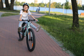 Positive girl child in a helmet rides a bicycle with her legs up.