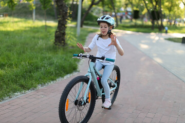 A cheerful little girl in a helmet is trying to ride a bicycle without hands.