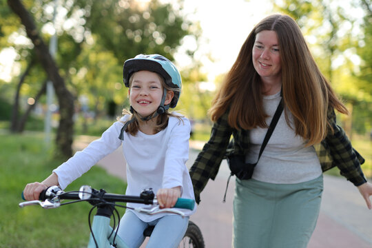 Happy Family Walk, Mom Teaches Child Daughter In A Helmet To Ride A Bike.