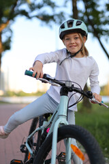 Portrait of a smiling girl in a helmet riding a bicycle in the park vertically.