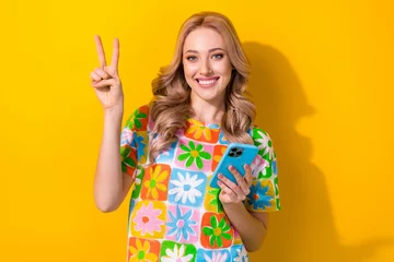 Fotobehang Photo of cute friendly woman dressed flower print t-shirt typing sms modern device showing v-sign isolated yellow color background © deagreez