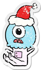 hand drawn distressed sticker cartoon of a cyclops alien spaceman wearing santa hat