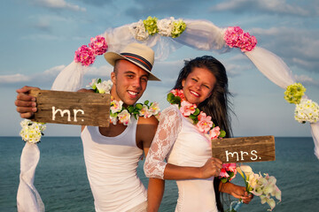 Groom with bride wearing lei, standing under archway on beach