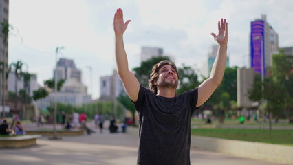 Fototapeta na wymiar Exultant Young Man Expressing Hope and Faith with Uplifted Arms Celebrating Triumph Outdoors in the Park