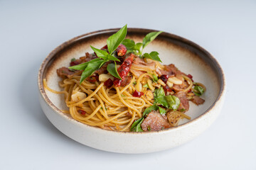 Spicy Thai basil pork pasta on white dish with white background. Italian food fusion Thai food. Tasty appetizing Italian fusion spicy spaghetti pasta with meat, chili, Thai basil. Italian fusion food.
