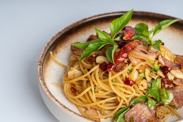 Close up Spicy Thai basil pork pasta on white dish, white background. Italian food fusion Thai food. Tasty appetizing Italian fusion spicy spaghetti pasta with meat, chili, Thai basil. Italian food