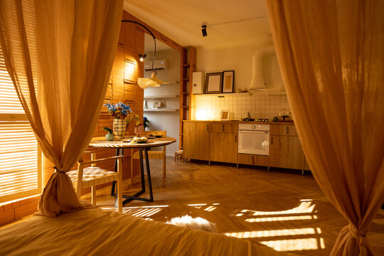 Sunny and cozy studio apartment with the sun's rays passing by the shutters. Interior made in warm tones with natural materials