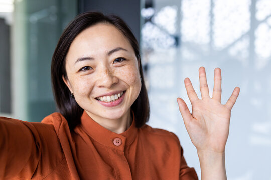 Business woman in the office talking on a video call, using application on smartphone for online remote communication, looking at the camera and smiling, asian inside .