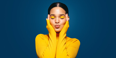 Radiating self-love: Young woman with colourful makeup embraces her face in a studio - obrazy, fototapety, plakaty