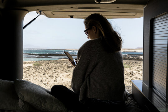 Unrecognizable woman traveler in camping van messing with mobile phone