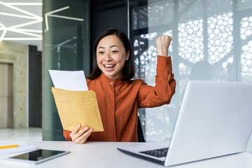 Fototapeta na wymiar Happy Asian business woman received letter from bank notification in envelope, happy business woman reading and reaching for good news, working inside office