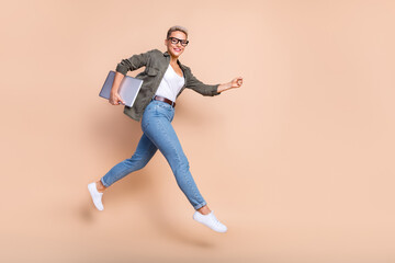 Fototapeta na wymiar Full length photo of cheerful sweet lady dressed khaki shirt jumping high modern device emtpy space isolated color background