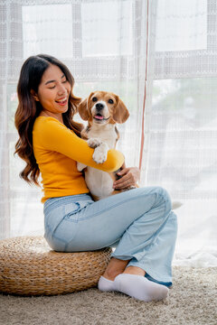 Vertical image young girl hold beagle dog and sit in front of glass door in her house and she look happy to play fun together.