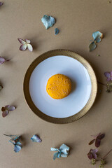 Orange macaron on a white and golden plate, against a neutral beige background with dried blooms