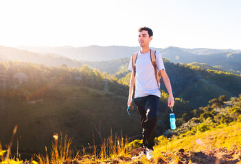 Naklejka premium Happy man walking high up on a mountain for exercise and relaxation while carrying a water bottle.