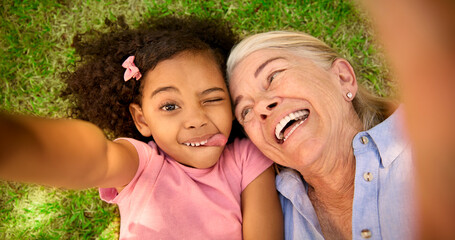 POV Overhead Shot Of Grandmother And Granddaughter Lying On Grass Taking Selfie On Mobile Phone