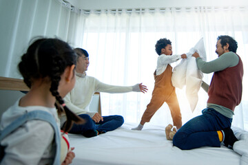 LGBTQ family, Male gay couple having fun with daughter and son on bed, fighting with pillows,...