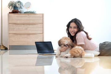 Teenage girl lying on the floor using laptop, Shih Tzu puppy and teen girl play fun at home, lovely...
