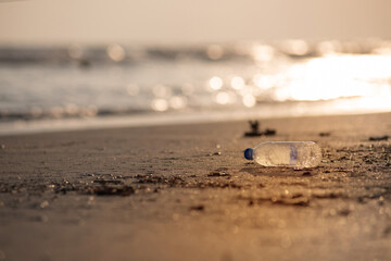 Waste plastic bottles that are dumped into the ocean will be brought to the beach by waves,  while the sunset in blurs the background, environmental pollution problems concept