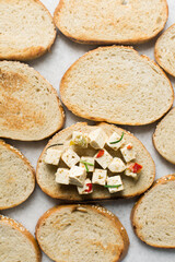 Top view of marinated feta cheese cubes on a slice of toasted bread. Cheese cubes with tomato and herbs on bread, flat lay of feta cheese on slice of toast