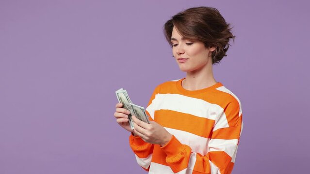 Happy happy fun rich accountant young woman wear casual clothes hold in hand count stack of cash money in dollar banknotes isolated on plain pastel light purple background. People lifestyle concept