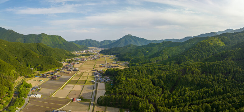 Lush green mountains surround rice fields and small farming village