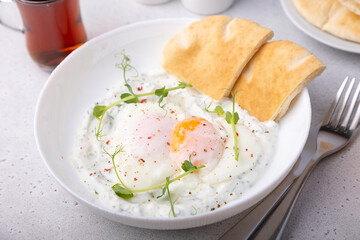 Turkish eggs (chilbir) with yogurt, fragrant butter, pea sprouts, flatbread and tea. Traditional Turkish breakfast with poached eggs (with liquid yolk). Selective focus, close-up