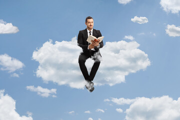 Businessman sitting on a cloud with a book