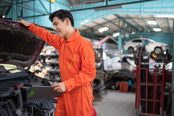 Fototapeta na wymiar Asia mechanic man examining and maintenance to engine a vehicle car hood with car lift background at car service 