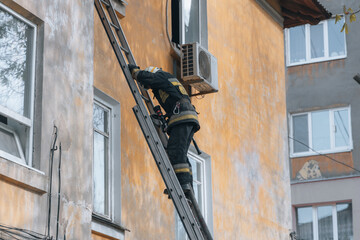 Fototapeta na wymiar View of a brave firefighter in a protective uniform. Rescuer in protective gear. Firefighters put out a fire in a residential building.