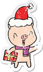 happy hand drawn distressed sticker cartoon of a pig with xmas present wearing santa hat