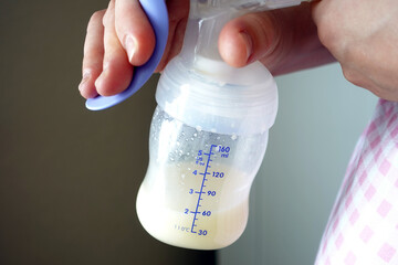 Close-up view of a mother using a manual breast pump with some breast milk in the bottle
