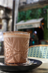 Hot Chocolate Drink Served in a Clear Glass With the Cafe as the Background
