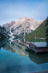 Grüner See in den Bergen mit Booten und einer Holzhütte mit glattem Wasser und Spiegelung zur blauen Stunde vor Sonnenaufgang.