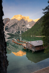 Grüner See in den Bergen mit Booten und einer Holzhütte mit glattem Wasser und Spiegelung zum Sonnenaufgang.