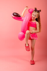 Happy joyful child girl in swimsuit having fun with swimming ring flamingo on a colored pink background. Summer beach concept