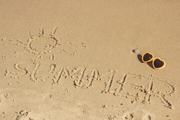 Inscription summer with shape of sun and sunglasses on sand at beach. Vacation time