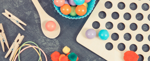 Colorful pompoms, balls and rubber erasers with spoon and tongs. Development of kids motor skills, coordination, creativity and logical thinking