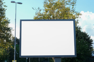 Blank advertising sign board display billboard mockup outside with trees and blue cloudy sky background. White billboard banner background in city. Selective focus of billboard.