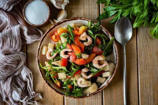 A dish for a romantic dinner: salad with shrimp, arugula, pear, tomatoes, garlic and olive oil in a beautiful plate on wooden boards. View from above