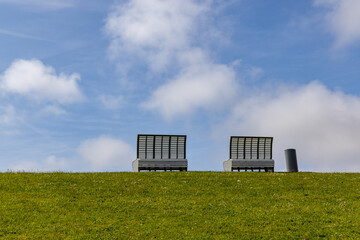 Two empty benches on top of the dike invite to take a seat mit view of the North Sea