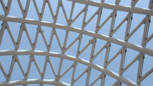 Close-up of a white metal arch with a glass roof against a beautiful blue sky.