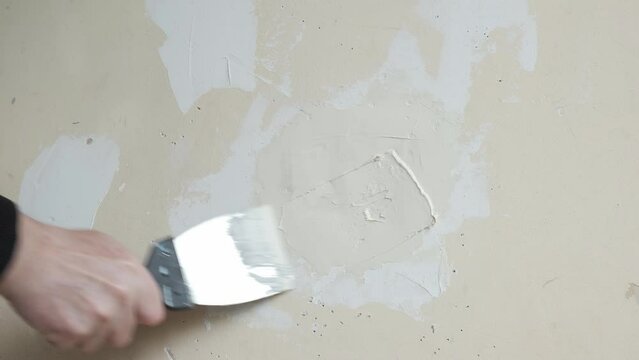 Close-up a man repairing crack white wall with spatula.