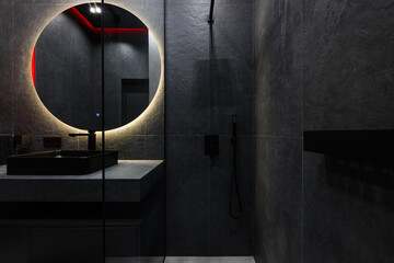 interior design of the bathroom in a modern version of dark tiles and lighting with a round mirror