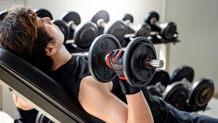 Sport man with well trained body in black sportswear doing incline dumbbell shoulder press on...