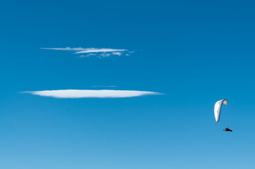 Vista de un parapente volando en un cielo limpio sólo roto por dos nubes.