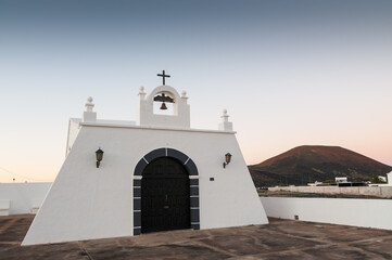 Fototapeta na wymiar Paisaje de Lanzarote, islas canarias, con una ermita blanca y un volcán al fondo.
